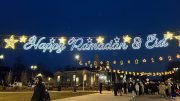 Celebratory lights spelling "happy Ramadan & eid" above a crowd gathered at dusk, embodying devotion and community during Ramadan 2024: A time for reflection.