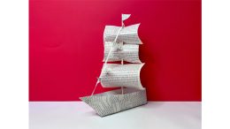 A paper ship made from printed text pages rests on a white surface with a bright red background, promoting the 2024 Monthly Wednesday movie night featuring "The Color Purple" at Milton Public Library on June 12.