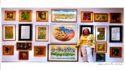 A woman standing beside a wall displaying various colorful framed paintings and sketches from the 'Making Waves' exhibit by Artist John Anthony Lawrence, with a signature and date in the corner.