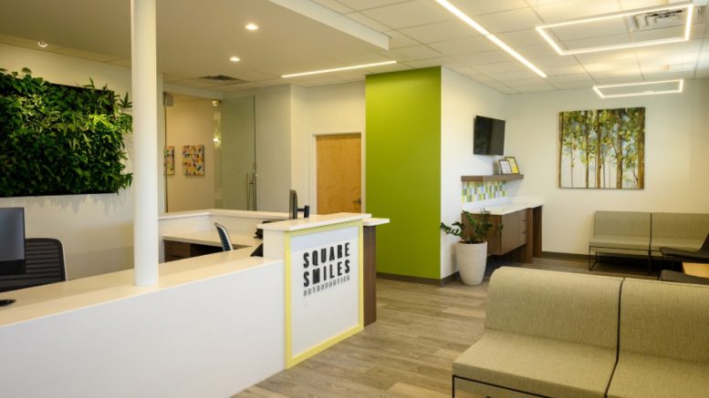 Reception area of Square Smiles Orthodontics in Milton MA, boasting a modern design with a green accent wall, stylish wall art, comfortable seating areas, and a reception desk displaying the name "Square Smiles Orthodontics". This welcoming space sets the stage for top-notch orthodontic care.