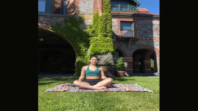 A woman sits cross-legged on a patterned blanket, meditating on a grassy lawn in front of a brick building with ivy-covered walls during the Juneteenth community celebration at Eustis Estate on June 22, 2024.