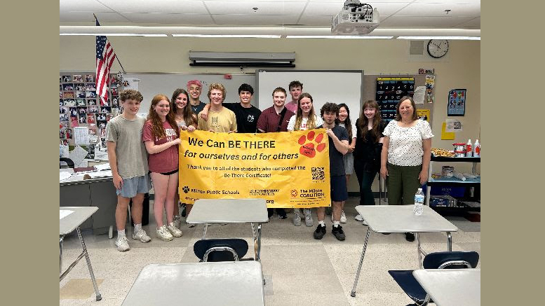 A group of Milton High students and a teacher stand in a classroom holding a banner that reads "We Can BE THERE for ourselves and for others." These dedicated advocates are joined by various logo sponsors as they push for stricter alcohol policies at the State House.