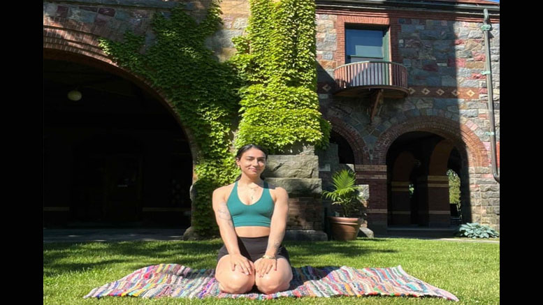A person sits on a colorful blanket on the grass in a meditative pose in front of a stone building with ivy-covered arches, preparing for the summer concert series Olson Pingrey Quartet at Eustis Estate on July 11, 2024.