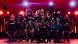A group of performers on stage in stylized, dark, glittery costumes, singing and dancing with bright stage lights in the background at the 2024 Milton Neighbors Choice Award hosted by Boxcar Stage Company.