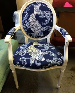 Upholstery by Michael: A white wooden chair with a round backrest and cushioned seat, both adorned in blue fabric upholstery featuring a delicate white koi fish design. This elegant piece of furniture brings a touch of serenity to any room.