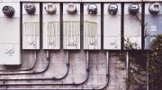 A row of utility meters mounted on an exterior wall, with green paint drips on some of them and vines growing from the bottom right corner—an everyday reminder that cutting utility costs can be one of those simple but effective business tips.