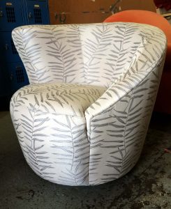 Upholstery by Michael: A gray and white patterned armchair with leaf motifs, part of the Upholstery By Michael collection, sits on a concrete floor in front of blue lockers and an orange chair.