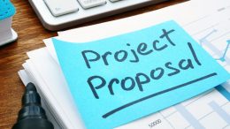 A stack of papers titled "Project Proposal" sits on a desk with a pen beside it, inviting ambitious ideas to breathe new life into the historic East Milton fire station.