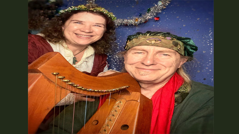 Two people in medieval-style attire pose with a wooden harp against a blue starry background decorated with tinsel, capturing the enchanting spirit of the upcoming holiday concert at Milton Art Center featuring Jennifer Kimball and Friends.