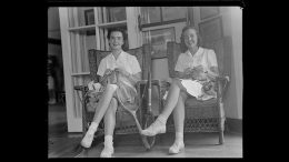 Two women in white dresses sit on wicker chairs, smiling and knitting as they discuss the Milton Public Library's adult programs for December 2024.