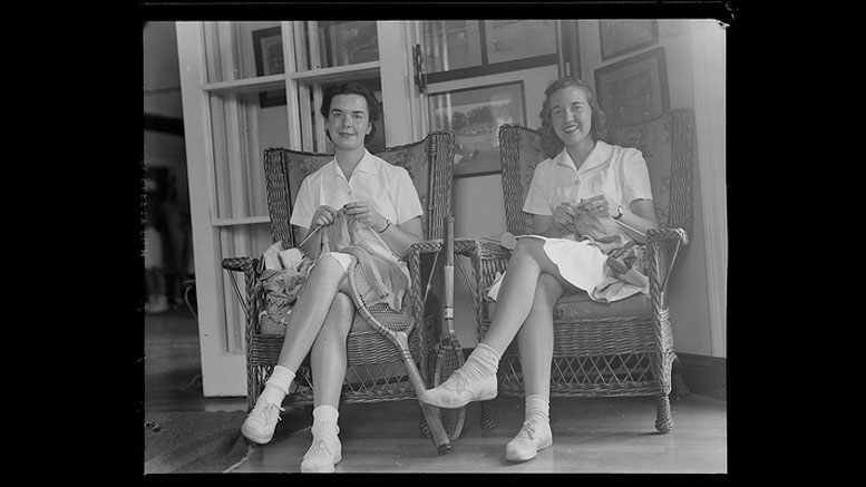 Two women in white dresses sit on wicker chairs, smiling and knitting as they discuss the Milton Public Library's adult programs for December 2024.