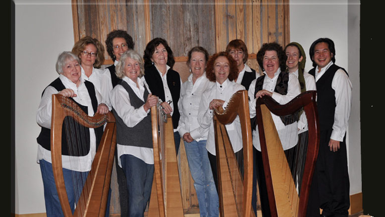 A group of eleven people poses with harps in front of a wooden backdrop, dressed in black and white attire, reminiscent of the elegance showcased at The Milton Public Library's adult programs announcement for December 2024.