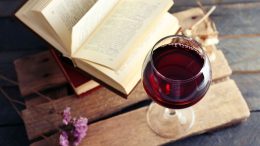 A glass of red wine sits on a wooden surface next to an open book, setting the scene for "Boozy Bookworms." Join us on November 21 for a fun-filled book club night!