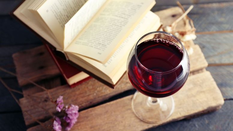 A glass of red wine sits on a wooden surface next to an open book, setting the scene for "Boozy Bookworms." Join us on November 21 for a fun-filled book club night!