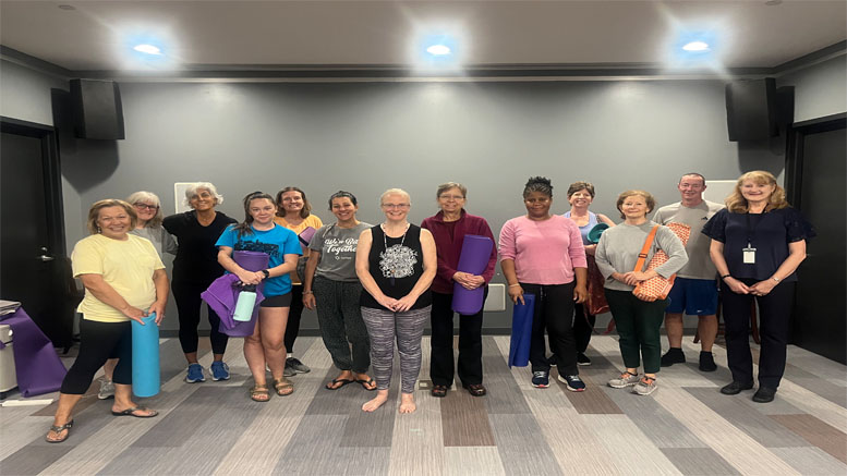 A group of people stands in a room at the Milton Public Library, holding yoga mats and wearing casual workout clothes, as part of the library's newly announced adult programs for January 2025.