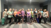 A group of women standing in a room, holding yoga mats and smiling at the camera, share their excitement for the upcoming wellness classes as part of The Milton Public Library's adult programs announced for February 2025.