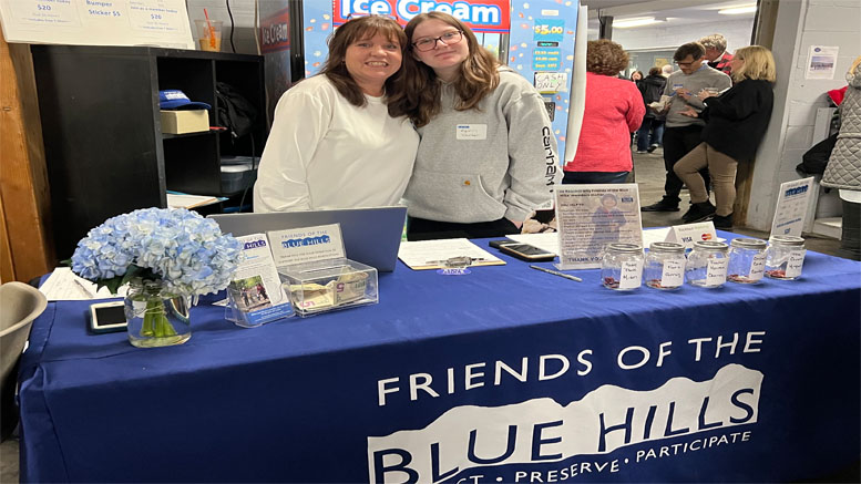 Two people stand behind a "Friends of the Blue Hills" table adorned with informational materials and donation jars, promoting the Friends of the Blue Hills Winterfest set for Tuesday, February 28.