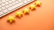 A row of five yellow star-shaped objects sits beside the edge of a silver keyboard on an orange surface, reminiscent of the insights found in Small Business Corner's tax tips to save you money in 2025.