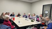 In a meeting room, a group of people sit around a rectangular table, smiling and exchanging items. As they unwind in this tranquil setting, you can almost imagine them gearing up for the "Find Your Calm: Chair Yoga at Milton Public Library" event on March 27, 2025.