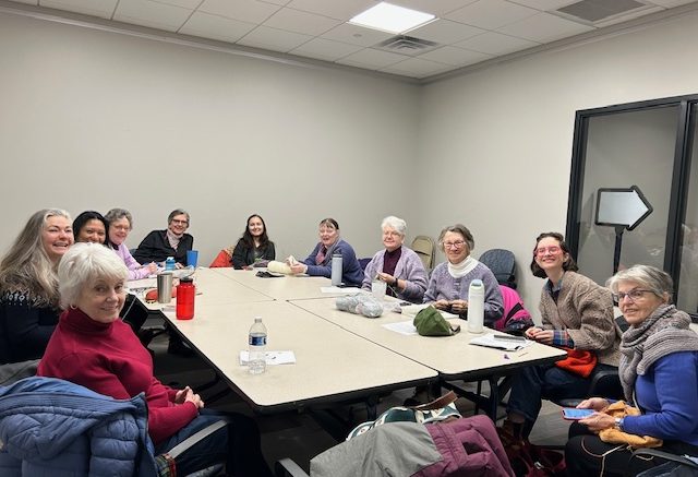 In a meeting room, a group of people sit around a rectangular table, smiling and exchanging items. As they unwind in this tranquil setting, you can almost imagine them gearing up for the "Find Your Calm: Chair Yoga at Milton Public Library" event on March 27, 2025.