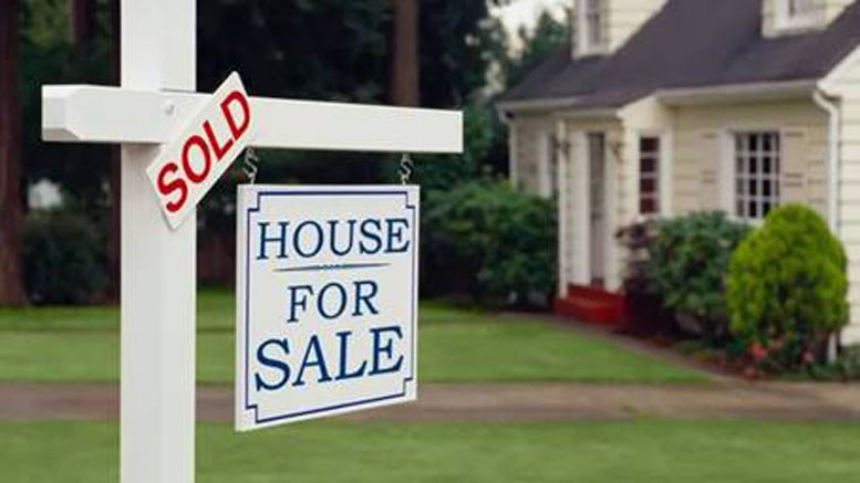 A "House For Sale" sign with a "Sold" label stands proudly in front of a charming white house, complete with a sloped roof and lush green lawn—a testament to the vibrant Norfolk County real estate activity on the rise in 2024.