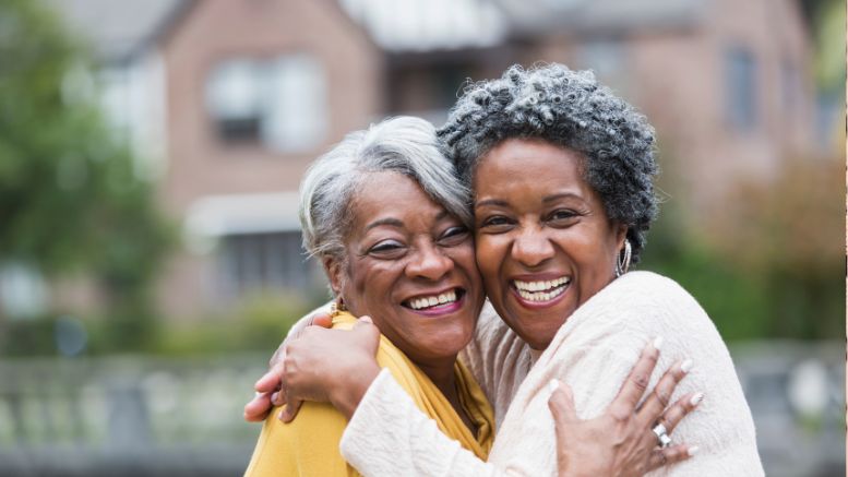 Two older women smiling and hugging outdoors with a house in the background, celebrating the Solo Agers Planning series. Don't miss the February Zoom sessions ahead!.