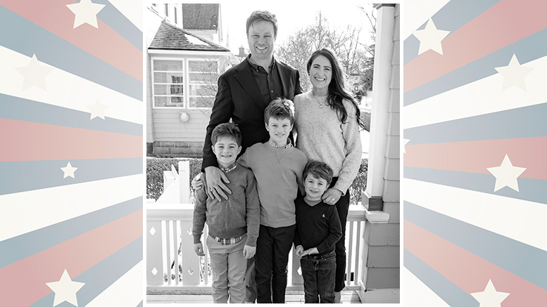 A family of five poses on a porch, consisting of two adults and three children. They are in front of a house. The image has a star-patterned border.